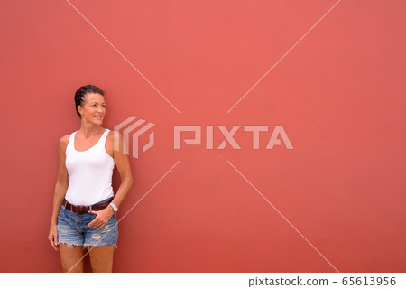 Happy mature beautiful tourist woman thinking against pink wall Happy mature beautiful tourist woman thinking against pink wall 65613956