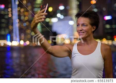 Happy mature beautiful tourist woman taking selfie in the city at night Happy mature beautiful tourist woman taking selfie in the city at night 65613973