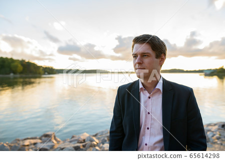 Young handsome businessman thinking in front of beautiful scenic shore Young handsome businessman thinking in front of beautiful scenic shore 65614298