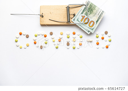 covid-19 inscription with pills and capsules and hundred dollar bill caught in a wooden mousetrap in layout on a white background copy space. Coronavirus, medicine and health, safety concept. covid-19 inscription with pills and capsules and hundred dollar bill caught in a wooden mousetrap in layout on a white background copy space. Coronavirus, medicine and health, safety concept. 65614727