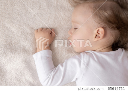 Childhood, sleep, rest, family, lifestyle concept - close-up portrait of a cute little boy of 2 years old in a white body sleeping on a beige bed at noon with mouth open top and side view. Childhood, sleep, rest, family, lifestyle concept - close-up portrait of a cute little boy of 2 years old in a white body sleeping on a beige bed at noon with mouth open top and side view. 65614731