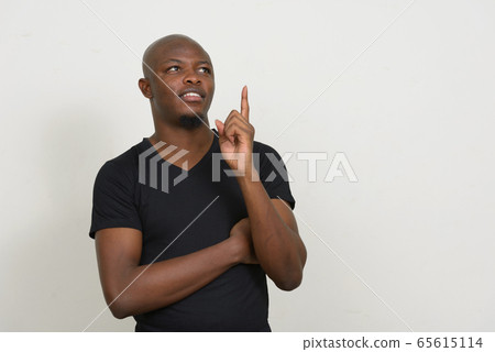 Happy young handsome bald African man thinking and pointing up Happy young handsome bald African man thinking and pointing up 65615114