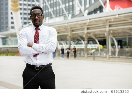 Young happy African businessman standing in front of modern building at Bangkok city 65615263