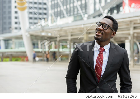 Young happy African businessman thinking in front of modern building at Bangkok city Young happy African businessman thinking in front of modern building at Bangkok city 65615269