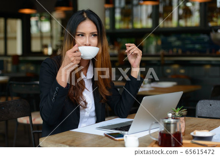Young beautiful Asian businesswoman drinking coffee at the coffee shop Young beautiful Asian businesswoman drinking coffee at the coffee shop 65615472