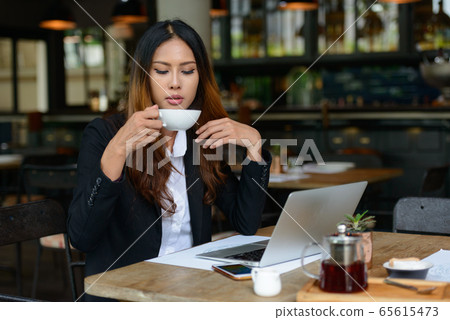 Young beautiful Asian businesswoman drinking coffee at the coffee shop Young beautiful Asian businesswoman drinking coffee at the coffee shop 65615473