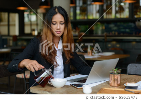 Young beautiful Asian businesswoman drinking coffee at the coffee shop Young beautiful Asian businesswoman drinking coffee at the coffee shop 65615475