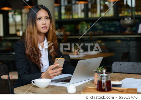 Young beautiful Asian businesswoman using phone at the coffee shop Young beautiful Asian businesswoman using phone at the coffee shop 65615476