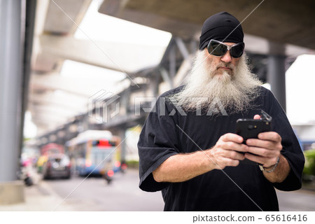 Mature bearded hipster man with sunglasses using phone in the city streets outdoors Mature bearded hipster man with sunglasses using phone in the city streets outdoors 65616416