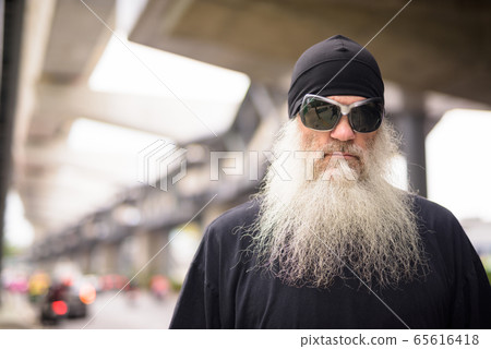 Face of mature bearded hipster man with sunglasses thinking in the city streets outdoors Face of mature bearded hipster man with sunglasses thinking in the city streets outdoors 65616418