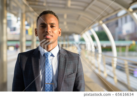 Happy young handsome African businessman in suit smiling in the city Happy young handsome African businessman in suit smiling in the city 65616634