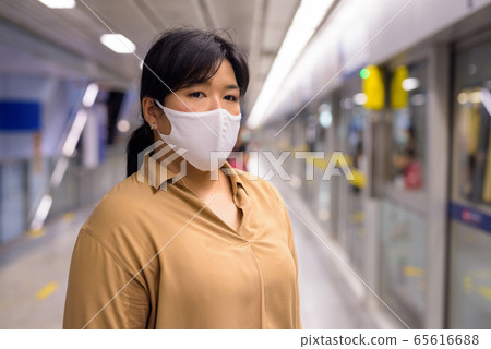 Overweight Asian woman waiting with mask for protection from corona virus outbreak at subway train Overweight Asian woman waiting with mask for protection from corona virus outbreak at subway train 65616688