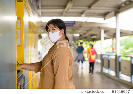 Overweight Asian woman with mask using self service locker box Overweight Asian woman with mask using self service locker box 65616697