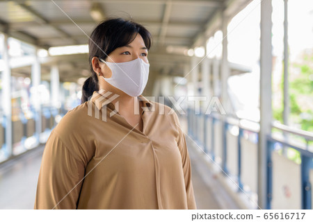 Overweight Asian woman thinking with mask for protection from corona virus outbreak at the Overweight Asian woman thinking with mask for protection from corona virus outbreak at the 65616717