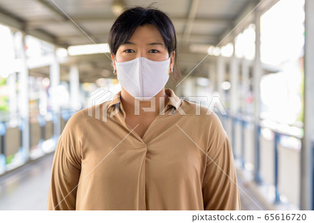 Overweight Asian woman with mask for protection from corona virus outbreak at the footbridge Overweight Asian woman with mask for protection from corona virus outbreak at the footbridge 65616720