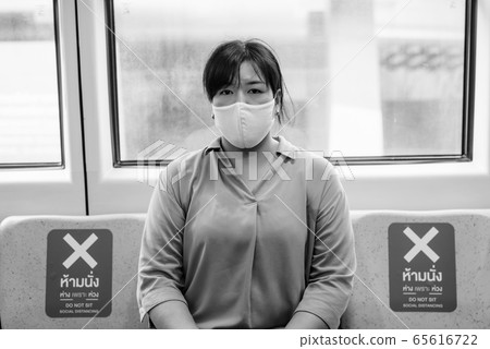 Overweight Asian woman with mask sitting with distance inside the train in black and white 65616722