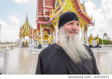 Face of happy mature bearded tourist man thinking at the Buddhist temple 65616971