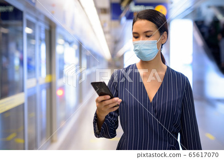Young Asian businesswoman with mask using phone while waiting at the subway train station Young Asian businesswoman with mask using phone while waiting at the subway train station 65617070