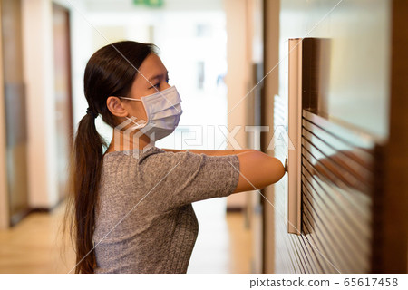 Young Asian woman with mask pressing elevator button with elbow for prevention of spreading the 65617458