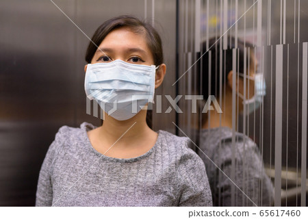 Young Asian woman with mask at corner of elevator for protection from corona virus outbreak 65617460