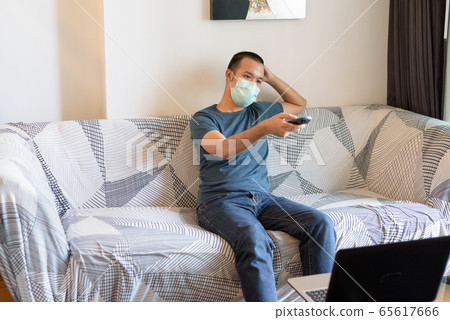 Young Asian man with mask watching tv at home under quarantine 65617666