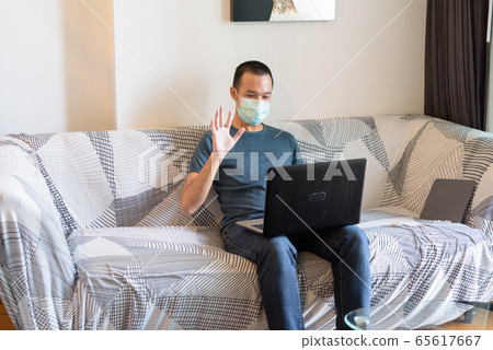 Young Asian man with mask video calling with laptop at home under quarantine 65617667
