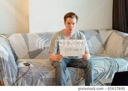 Young handsome man showing Stay At Home sign while under quarantine at home due to covid-19 pandemic Young handsome man showing Stay At Home sign while under quarantine at home due to covid-19 pandemic 65617690
