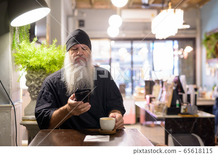 Serious mature bearded hipster man using phone at the coffee shop 65618115