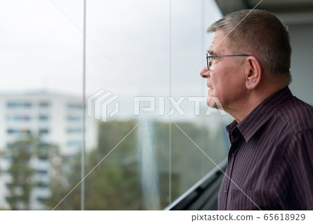 Profile view of old man thinking while looking outside glass window of modern building Profile view of old man thinking while looking outside glass window of modern building 65618929