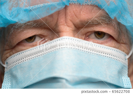 Close up portrait of sad senior adult dressed in surgical face mask with ear straps, covering nose from SARS, virulently infectious disease corona virus 65622708