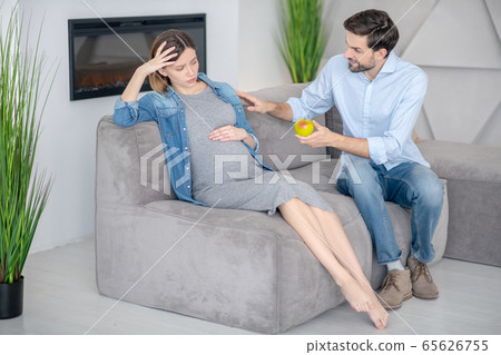 Young bearded man offering apple to his upset wife and smiling Young bearded man offering apple to his upset wife and smiling 65626755