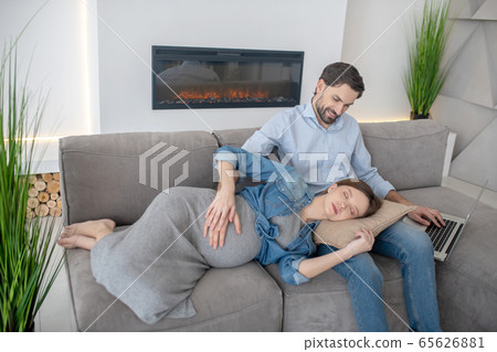 Young pregnant woman in a jeans jacket feeling sleepy laying on her husbands laps 65626881