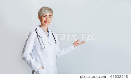 Woman invites to meet. Smiling doctor in white coat shows gesture welcome 65632948