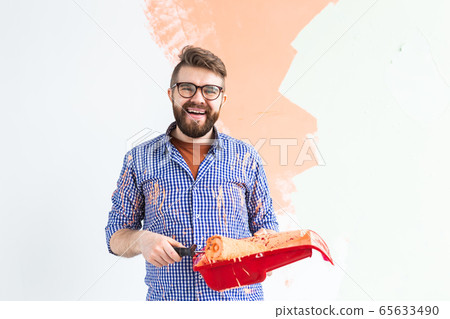 Renovation, redecoration and repair concept - Cheerful guy painting wall in new home. 65633490