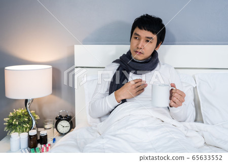 sick man drinking a cup of hot water on bed 65633552