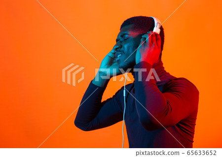 Young african-american man's listening to music in headphones in neon light. Male portrait. Concept of human emotions, facial expression, holidays or weekend, hobby, 65633652