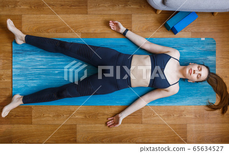 Young yogi woman relaxing in shavasana pose home 65634527