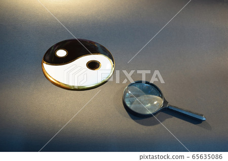 Yin yang symbol and magnifying glass on black brown background Yin yang symbol and magnifying glass on black brown background 65635086