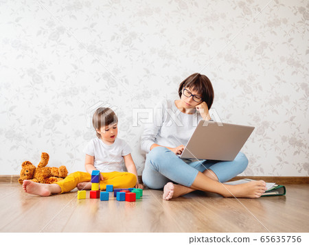 Mom and son sit at home quarantine because of coronavirus COVID19. Mother remote works with laptop, son plays with toy blocks. Self isolation at home. Mom and son sit at home quarantine because of coronavirus COVID19. Mother remote works with laptop, son plays with toy blocks. Self isolation at home. 65635756