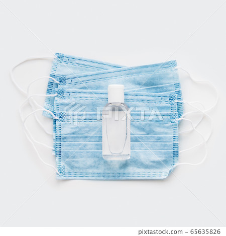 Top view on pack of blue protective medical masks with transparent bottle of sanitizer. Coronavirus COVID-19 concept on white background with copy space. Top view on pack of blue protective medical masks with transparent bottle of sanitizer. Coronavirus COVID-19 concept on white background with copy space. 65635826