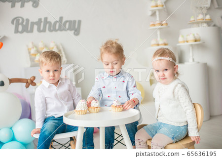 Cute little boys and girl at a table with birthday cakes at a children's party with balloons. Children's party. Balloons Cute little boys and girl at a table with birthday cakes at a children's party with balloons. Children's party. Balloons 65636195