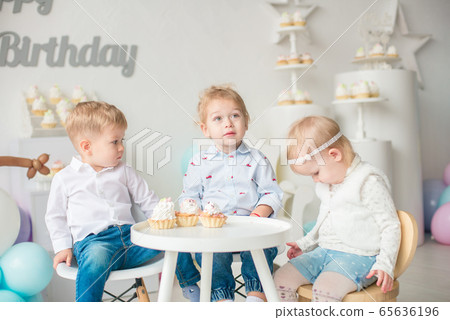 Cute little boys and girl at a table with birthday cakes at a children's party with balloons. Children's party. Balloons Cute little boys and girl at a table with birthday cakes at a children's party with balloons. Children's party. Balloons 65636196
