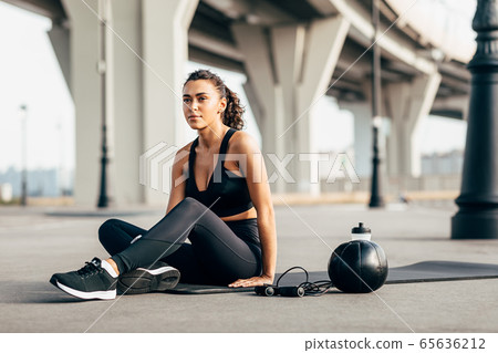 Woman in sportswear resting on mat after workout on city street 65636212