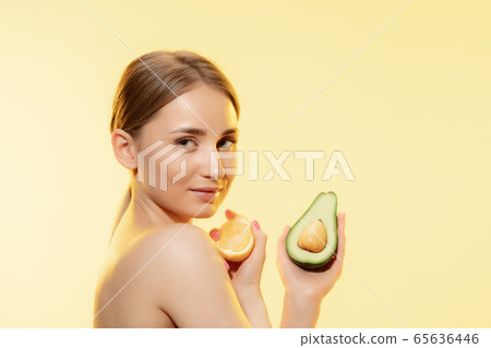 Vitamins splash. Close up of beautiful female face with lemon and avocado halfs over yellow background. Cosmetics and makeup, natural and eco treatment, skin care. Vitamins splash. Close up of beautiful female face with lemon and avocado halfs over yellow background. Cosmetics and makeup, natural and eco treatment, skin care. 65636446