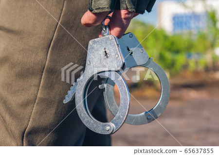 Handcuffs in the hands of a policeman close-up. Police equipment part Handcuffs in the hands of a policeman close-up. Police equipment part 65637855