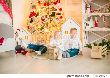 Cute little boys  with blond hair plays with little girl  in a bright room decorated with Christmas garlands near the Christmas tree. Happy childhood. Christmas mood 65639073