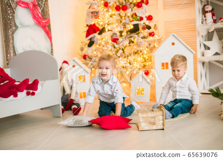 Cute little boys  with blond hair plays with little girl  in a bright room decorated with Christmas garlands near the Christmas tree. Happy childhood. Christmas mood 65639076