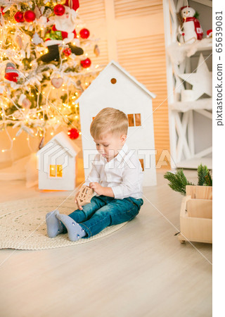 Cute little boy with blond hair plays with  toys in a bright room decorated with Christmas garlands near the Christmas tree. Happy childhood. Christmas mood 65639081