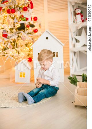 Cute little boy with blond hair plays with  toys in a bright room decorated with Christmas garlands near the Christmas tree. Happy childhood. Christmas mood 65639082