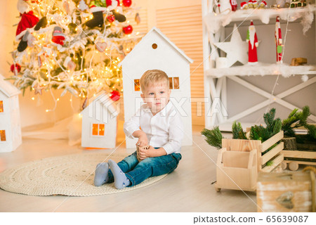 Cute little boy with blond hair plays with  toys in a bright room decorated with Christmas garlands near the Christmas tree. Happy childhood. Christmas mood 65639087